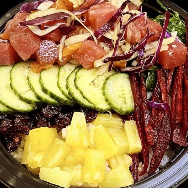 Close-up of a colorful poke bowl with tuna, cucumber, pineapple, and red cabbage.