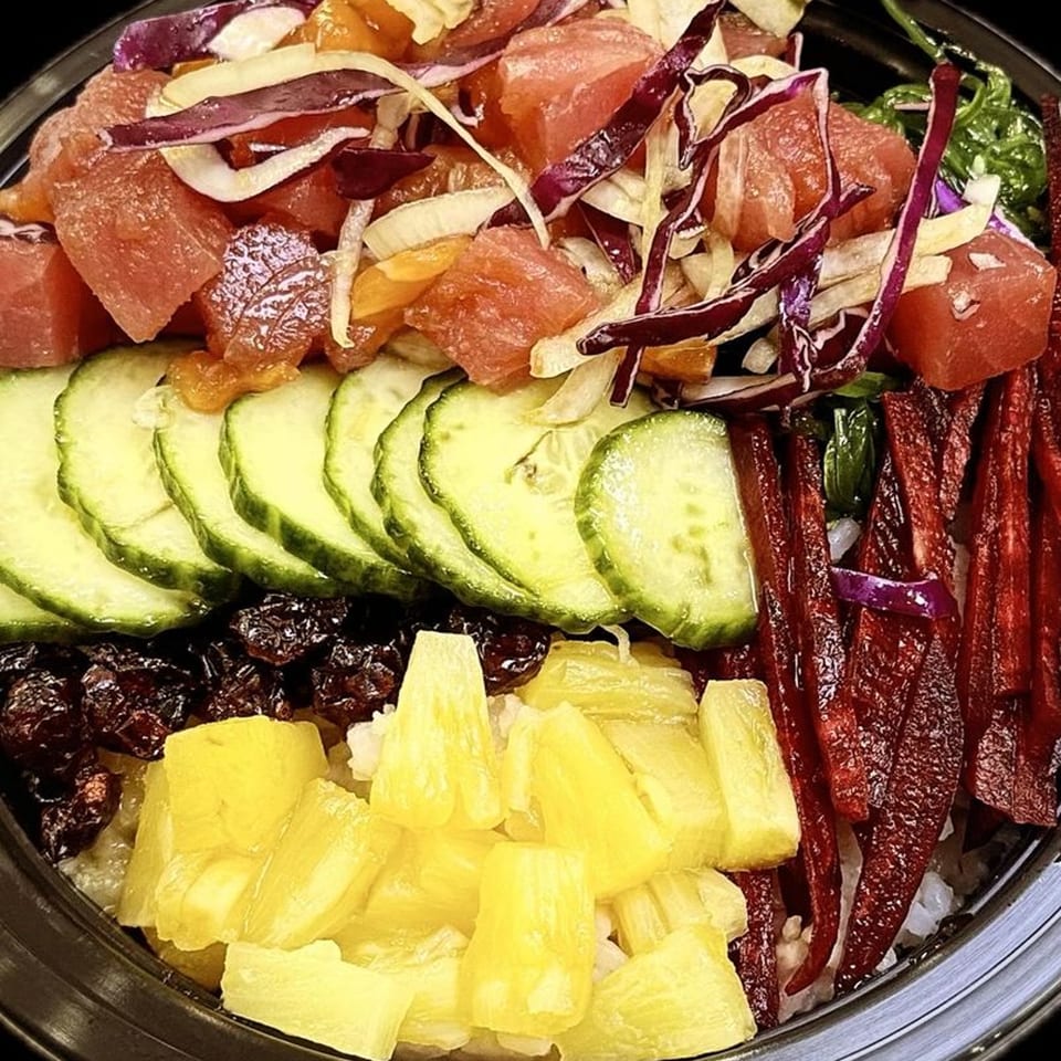 Close-up of a colorful poke bowl with tuna, cucumber, pineapple, and red cabbage.