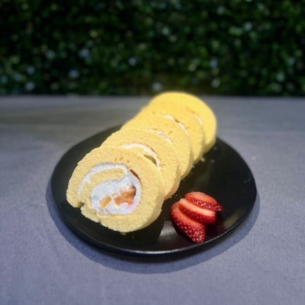 Sliced strawberry roll cake with cream filling and fresh strawberries on a black plate.