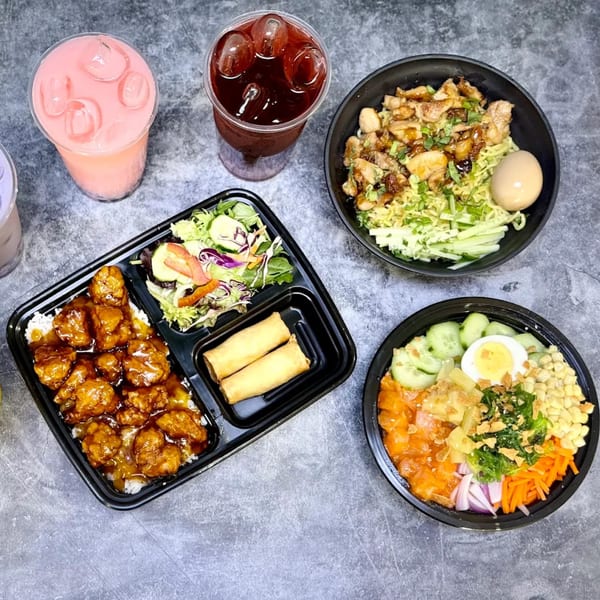 Two poke bowls, a chicken entree with rice and egg rolls, and two iced drinks on a gray surface.