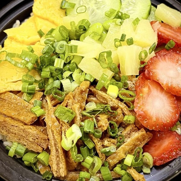 Close-up of a vibrant poke bowl with strawberries, pineapple, cucumber, egg, and green onions.